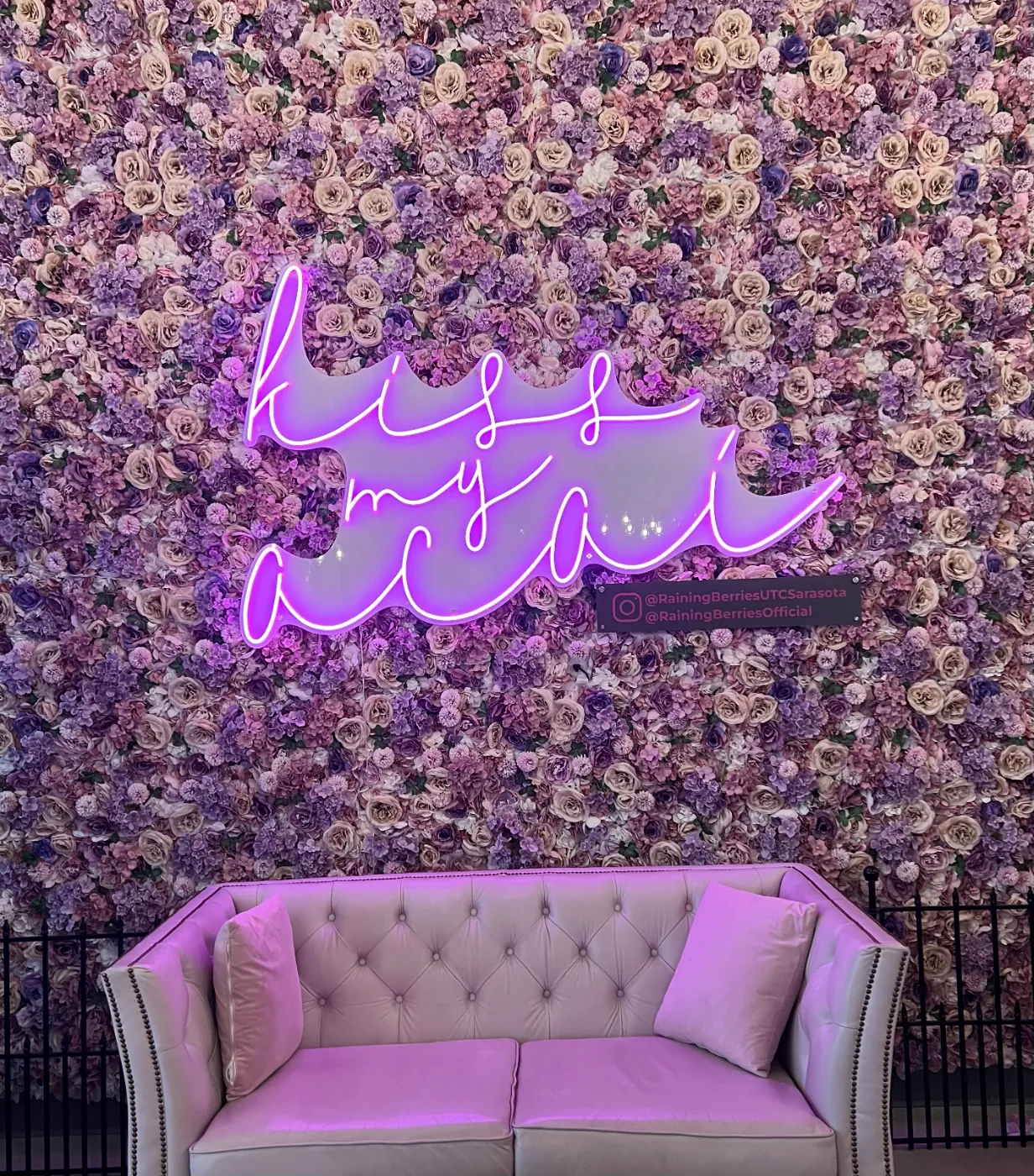 Kiss my açaí neon sign on a flower wall at Raining Berries